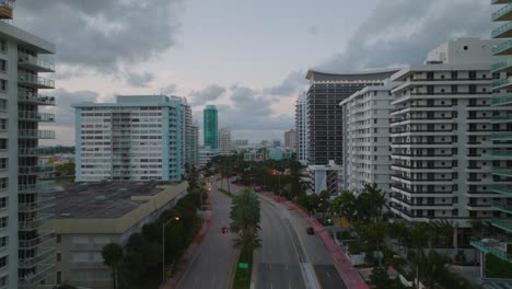 backwards revealing modern buildings along multilane trunk road in city at twilight. high rise apartment buildings with balconies. miami, usa