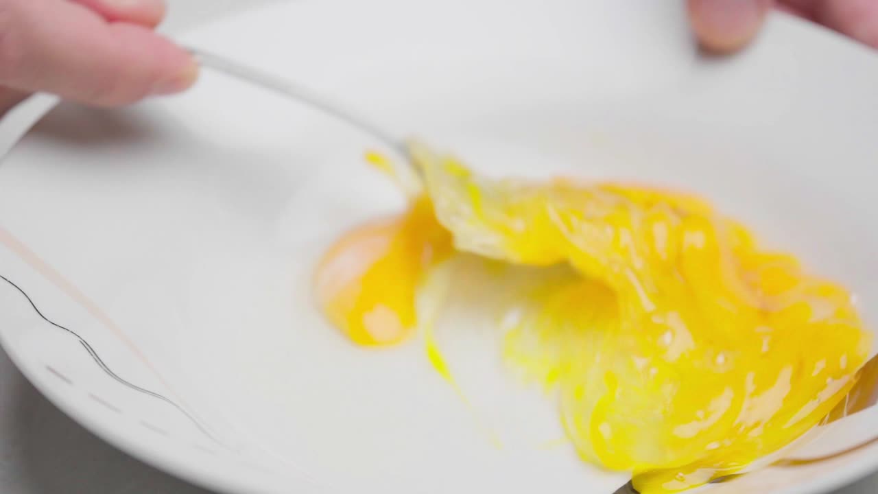 Slow-motion close-up of two raw eggs being mixed with a fork in a white bowl
