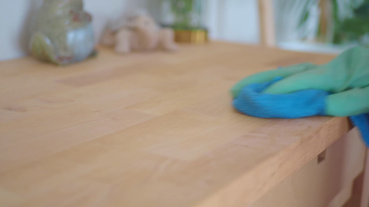 Hand in Green Glove Wiping Wooden Surface with Blue Cloth