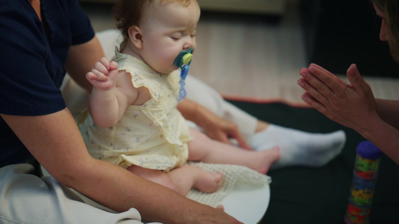 Close up overhead footage of a baby's legs and feet resting on an adult's lap during a calm indoor therapy or caregiving moment