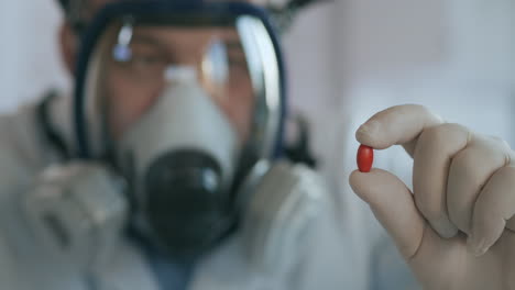 close up in the laboratory a man in a glass respirator screen holds a new medicine a red pill an antibiotic against the virus and looks at it. high quality 4k footage