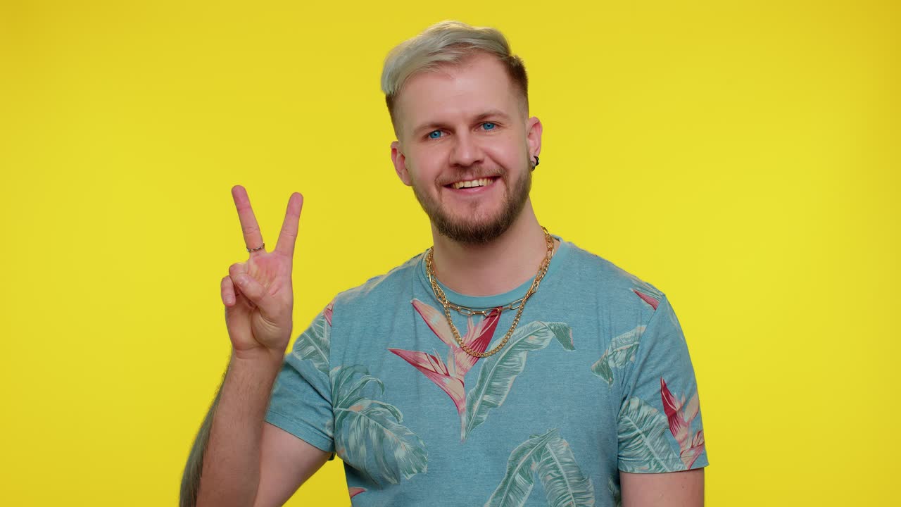 Uomo bello, elegante e sorridente che mostra il segno della vittoria, sperando nel successo e facendo il gesto della pace