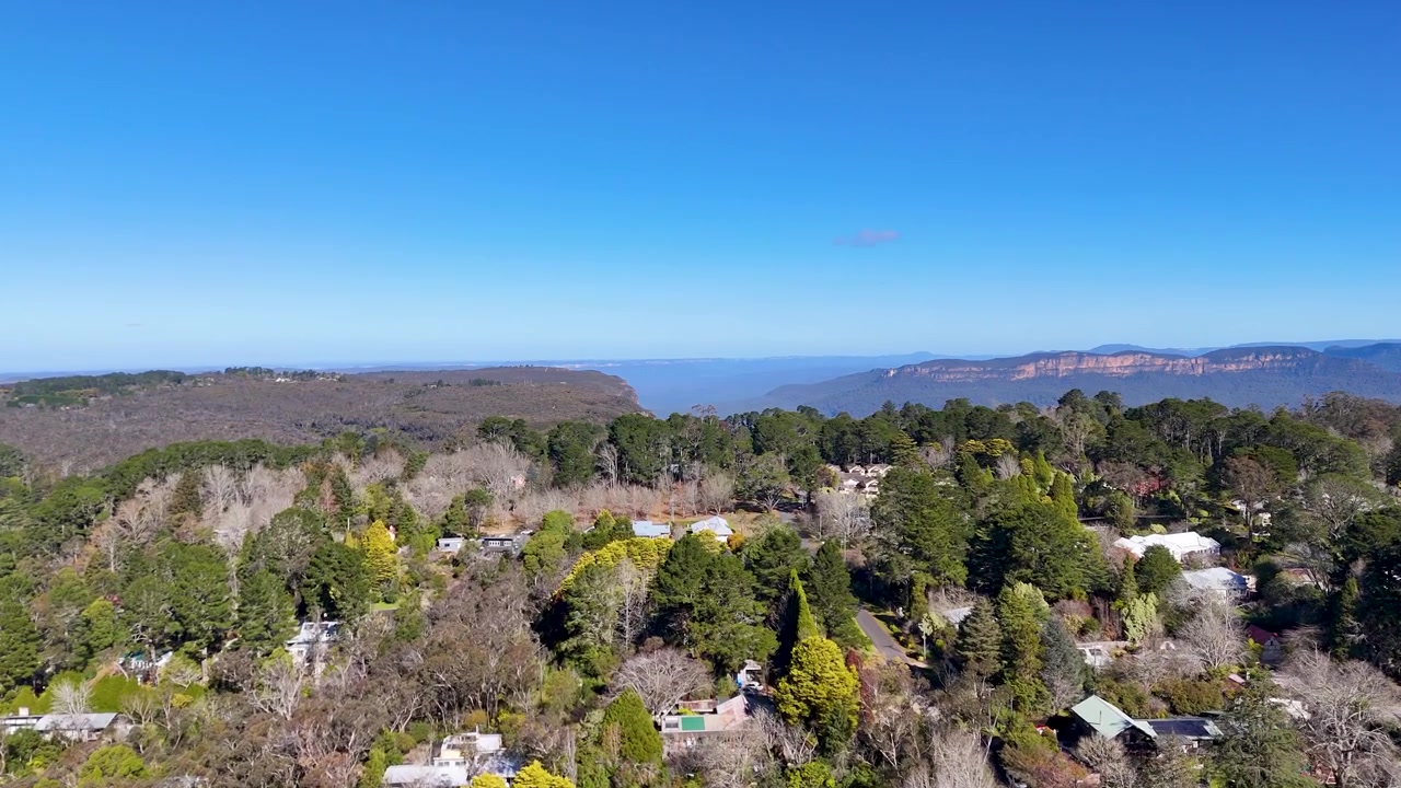 Bredt luftfoto af Jamison Valley eukalyptusskov og sandstensklipper under klar blå himmel.
