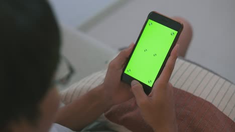 joven sentado en un sofá usando un teléfono inteligente con una pantalla de maquillaje verde