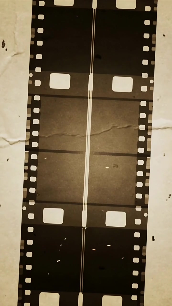 Video verticale: Telecamera che riprende una pellicola da 35mm che si inclina su un foglio bianco sporco, mostrando fotogrammi vuoti.