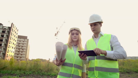 ingeniero adulto hombre y arquitecto mujer utiliza una tableta en funcionamiento. escribe un mensaje o revisa un dibujo. en el fondo está la construcción. vea el vecindario y los dibujos para la verificación de las obras de construcción completadas y planeadas. el trabajo de una grúa