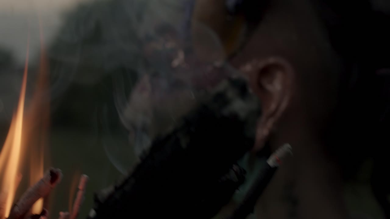 por la noche, un alguien con pintura facial beltane está sosteniendo una antorcha humeante, hay árboles en el fondo, y el cielo está oscuro