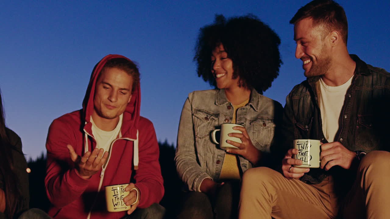 친구 들 이 캠프 불 에서 음료 를 즐기고 있다