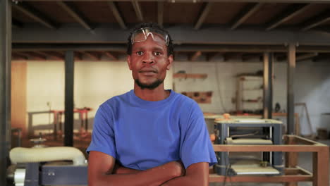 mid adult african american craftsman crossing arms and smiling while lowering goggles in workshop