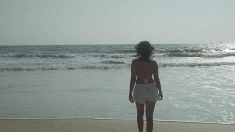 woman with dark hair walking away from camera into gentle lapping waves on shoreline