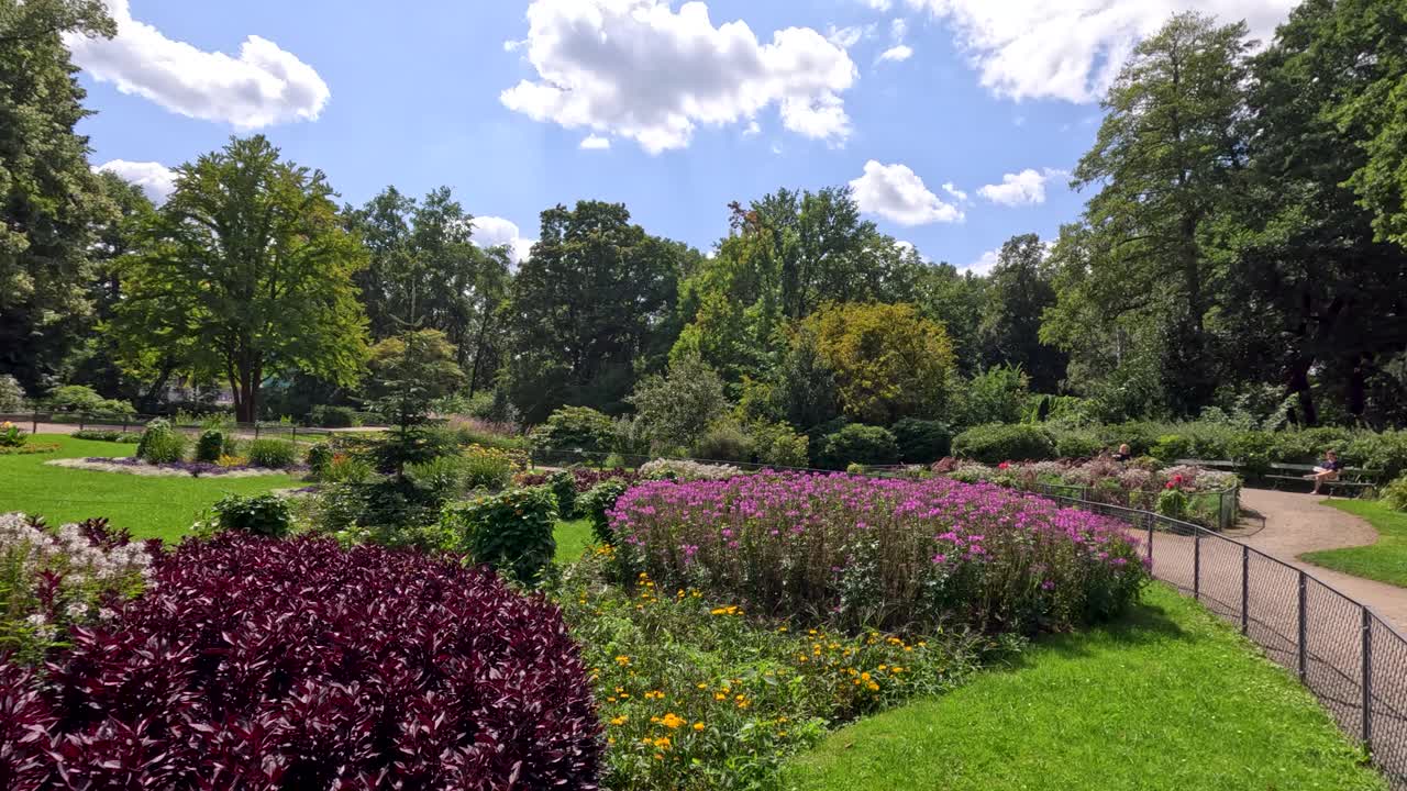 Daytime camera pan reveals vibrant flower beds, lush greenery, and mature trees in a landscaped Berlin park under bright, natural sunlight