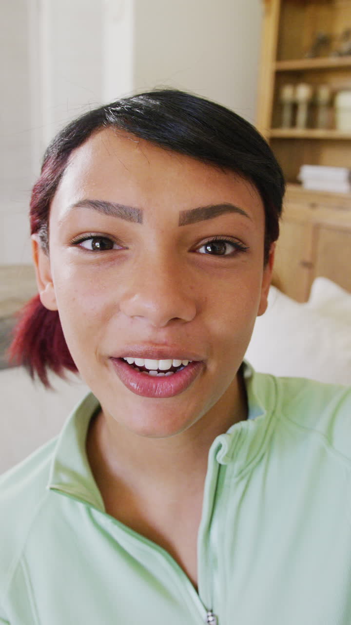 Vertical video of biracial teenager girl sitting on sofa and having video call, in slow motion