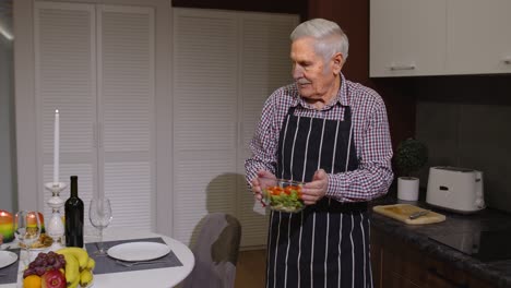 Old-elderly-man-cooking-for-his-wife-a-romantic-supper-with-wine-and-candles.-Senior-couple-in-love