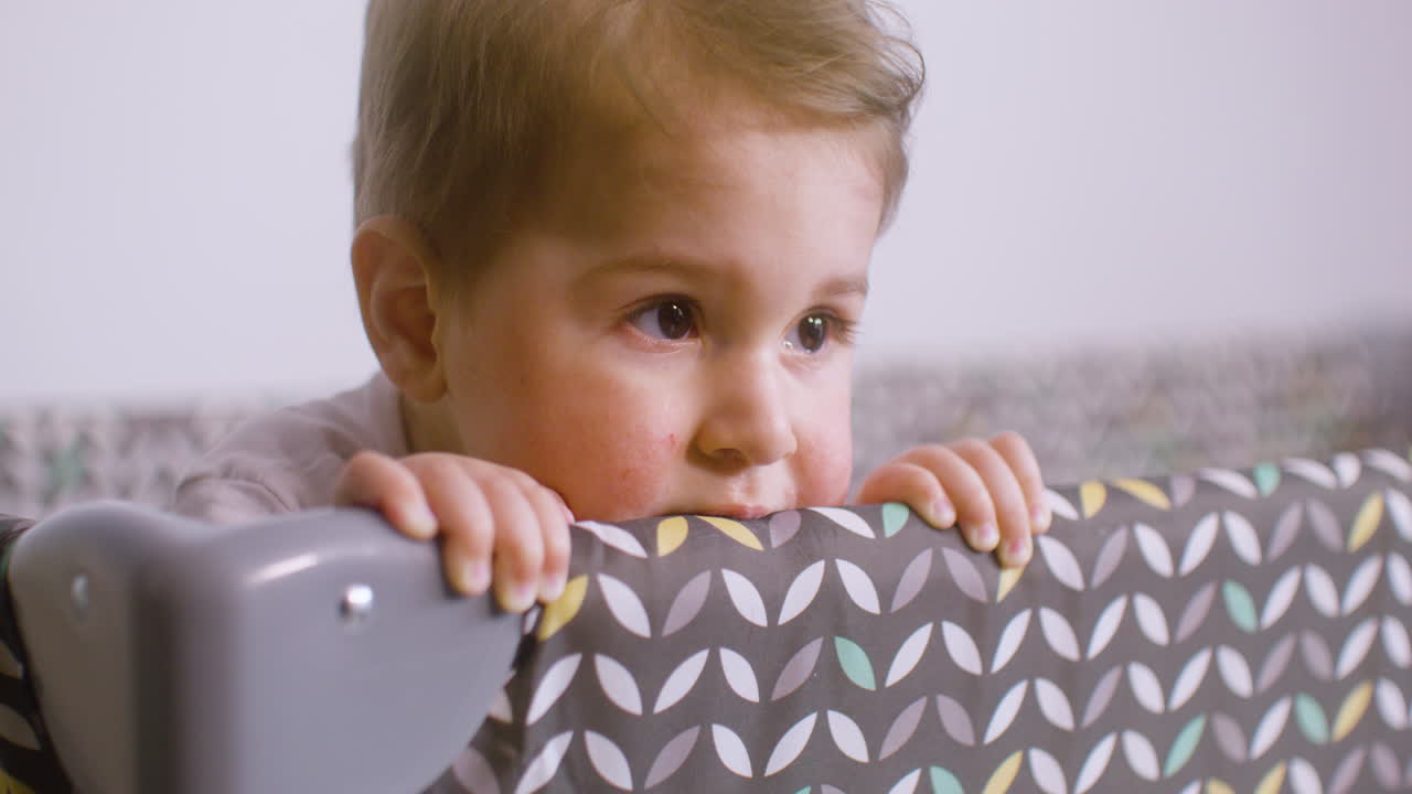 bebé con traje blanco dentro del parque infantil mientras muerde la tela del parque