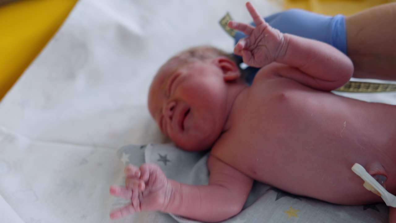 Newborn cries and waves his hands while being checked by the doctor. Medic uses measuring tape to know child's length. Close up.