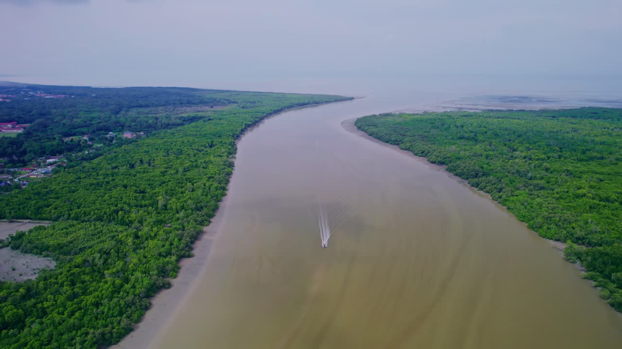 Wide drone shot of a boat traveling along a broad river with green foliage lining the banks