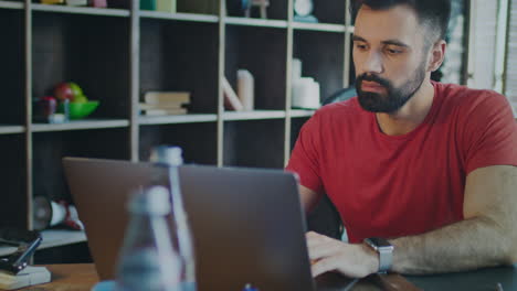 hombre con barba trabajando en una computadora portátil en la oficina de su casa. hombre mirando la pantalla de la computadora portátil