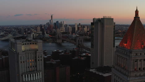 Fly-between-high-rise-buildings-in-Civic-Center-neighbourhood-of-Lower-Manhattan-at-dusk.-Aerial-view-of-bridges-to-Brooklyn.-Manhattan,-New-York-City,-USA
