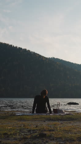 la mujer gira la cabeza para relajarse junto al lago al atardecer. la señora trata de sentir relajación en un picnic con vista a las montañas después de una semana dura. fin de semana tranquila sola