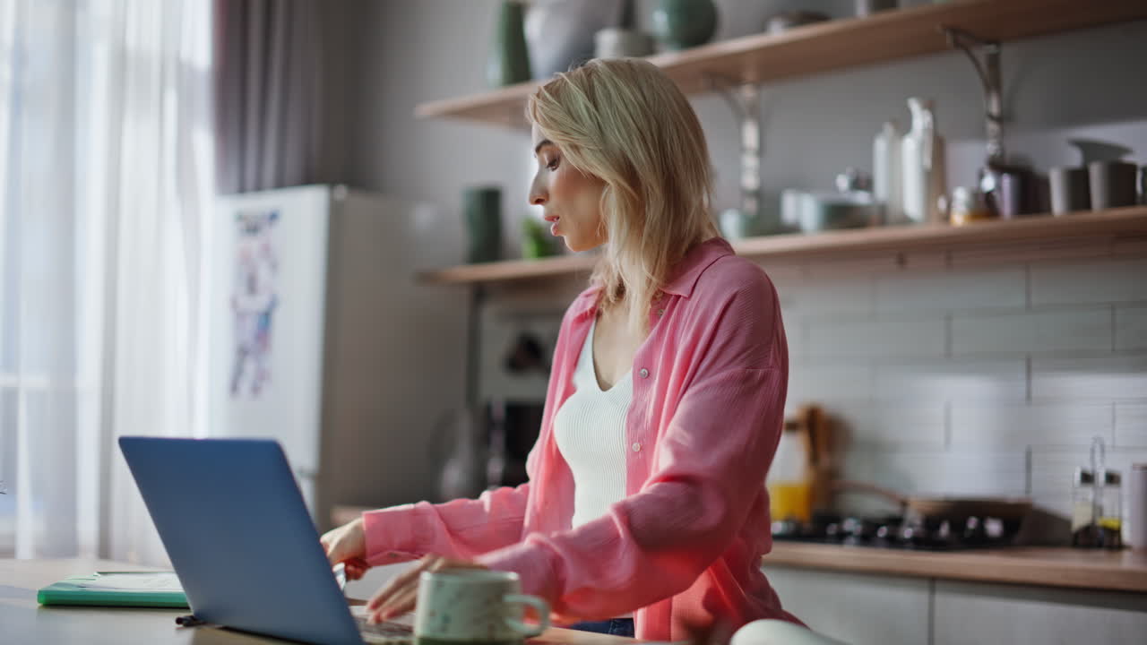 Freelancer typing laptop countertop home kitchen. Blonde analyzing documents