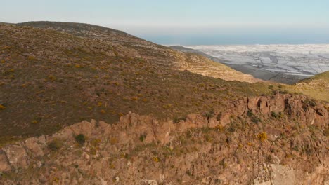 The-mountains-near-Almeria-in-the-south-of-Spain-with-in-the-background-the-greenhouses,-Aerial-shot