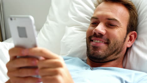 hombre sonriendo y usando el teléfono inteligente en la cama