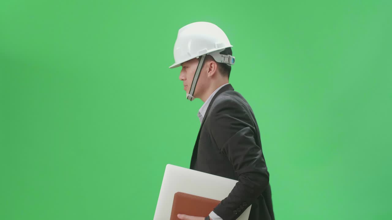 Side View Of Asian Chief Engineer In The Hard Hat Holding Book And Document While Walking On Green Screen Chroma Key