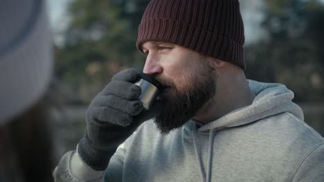 Close-up-of-caucasian-drinking-hot-tea-in-the-winter-outdoors-and-talking-with-unrecognizable-person.