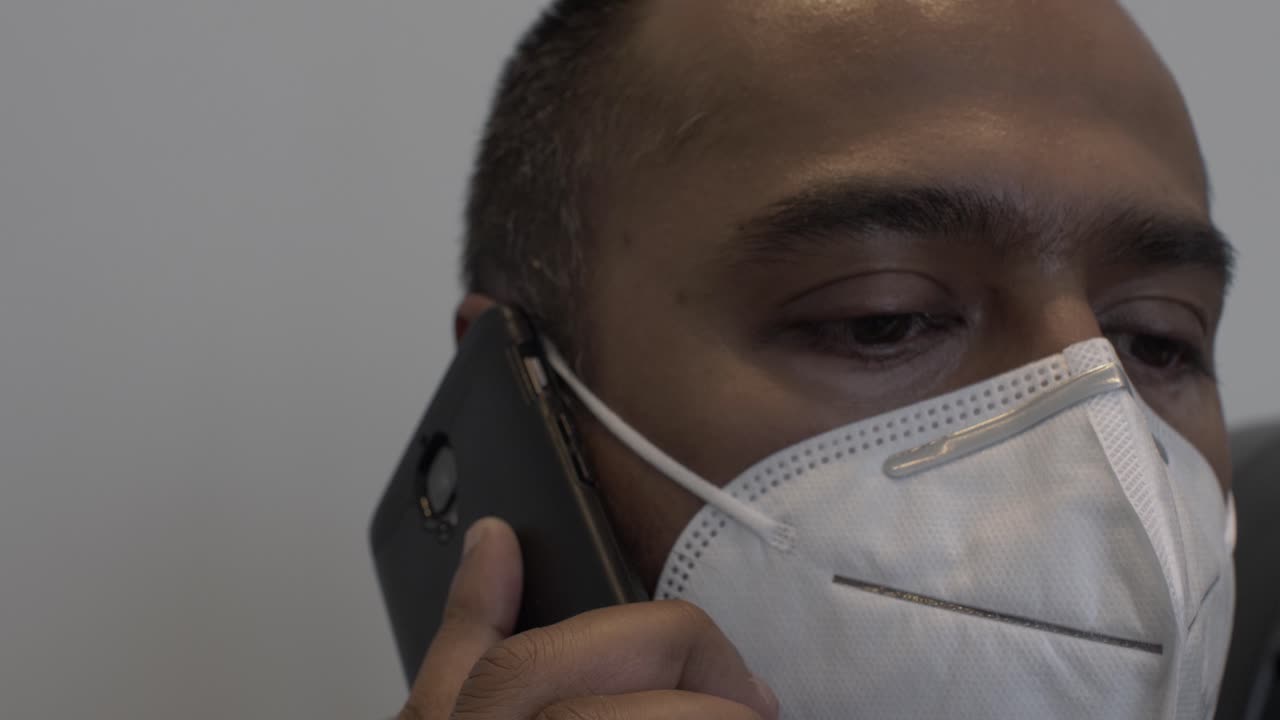 hombre asiático adulto con mascarilla n95 en interiores hablando por teléfono móvil
