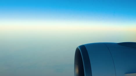 airplane flying over the clouds under clear blue sky. window view showing engine.