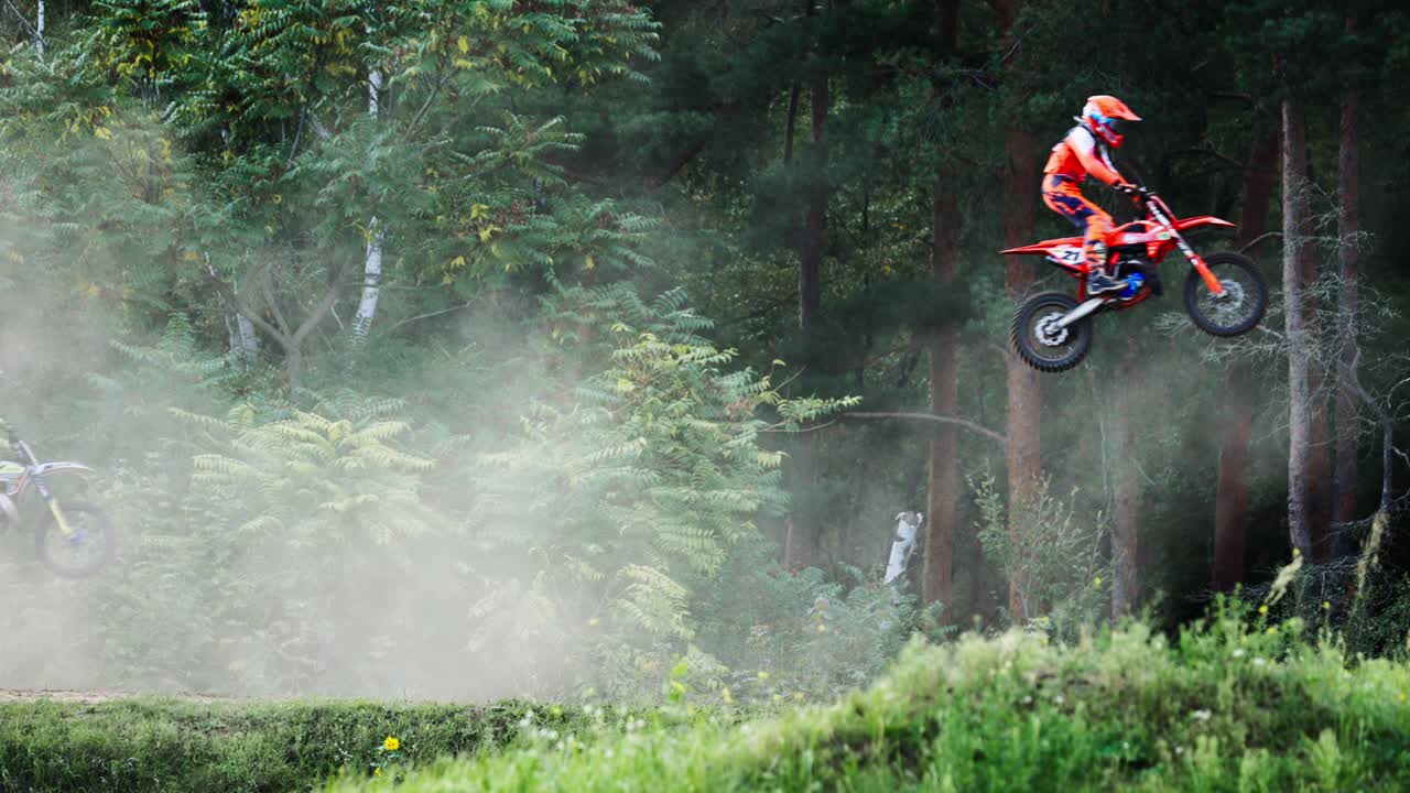 Grupo de Pilotos de Motocross Saltando no Ar Um por Um na Corrida em Terreno de Floresta