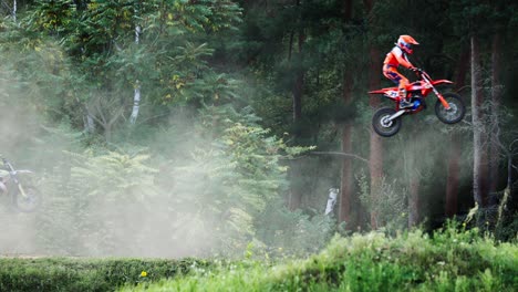 group of motocross riders jumping into air one by one at the forest terrain race