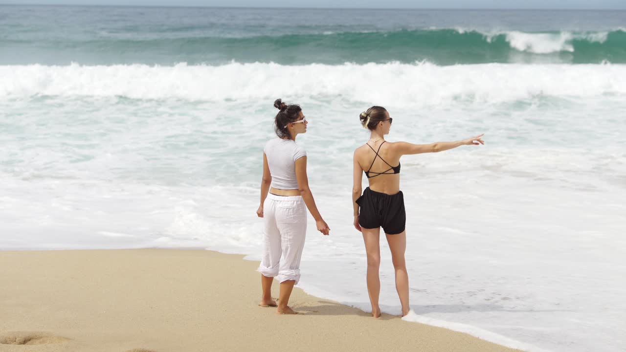 Two women on a sandy beach watching ocean waves
