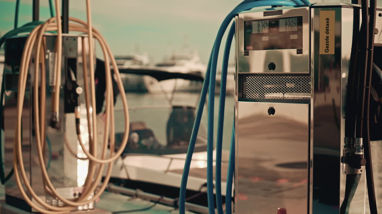Various hoses coloured in yellow, green, and blue, hang beside modern marina fuel pumps, boat at the fuel station