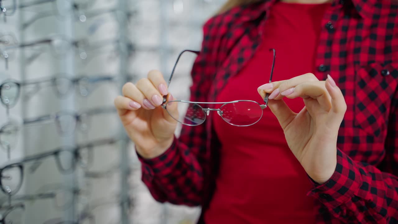 Stylish eyeglasses in woman's hands. Female buyer holding new spectacles in the optical store. Close-up.
