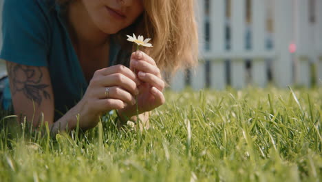 woman lying in grass observing a daisy
