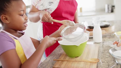 happy unaltered african american mother and daughter baking in kitchen, in slow motion