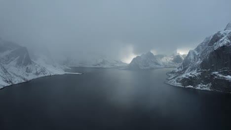 enchanting drone flight over the ocean in reine, norway, featuring snowfall, snow-covered mountains, and a cloudy sky