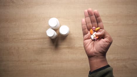 mano sosteniendo varias pastillas y botellas de medicamentos en una mesa.