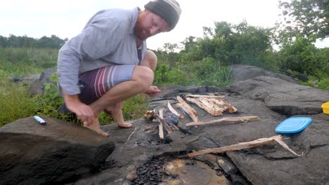 Un-Hombre-Iniciando-Un-Fuego-De-Campamento-En-El-África-Rural-A-Orillas-Del-Lago-Victoria