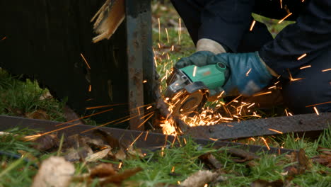 trabajador que usa molinillo creando chispas brillantes en metal viejo mientras usa guantes protectores y overoles