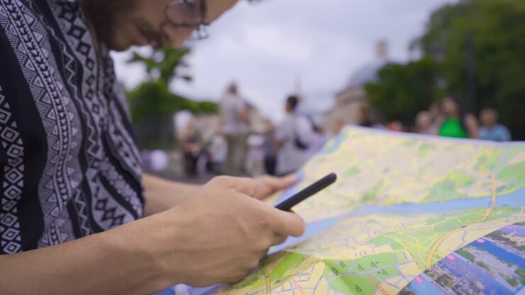 Young man tries to find the right way by looking at paper map and phone.