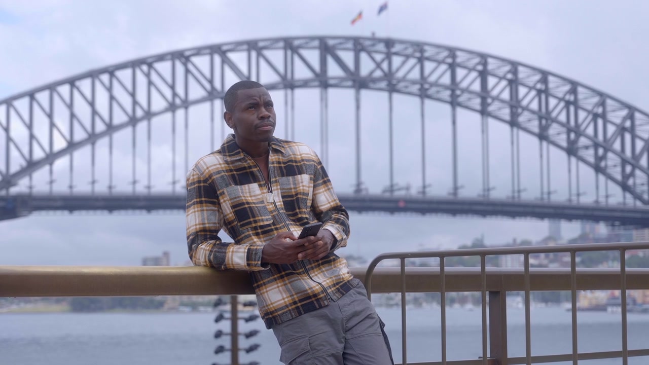 Il Sydney Harbour Bridge come sfondo per un ragazzo che aspetta e controlla il cellulare in Australia - Sydney