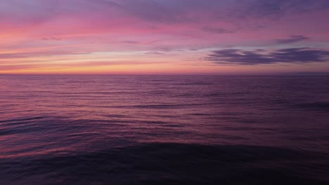 violet sunset reflecting in sea waves, aerial tilt up close to water surface