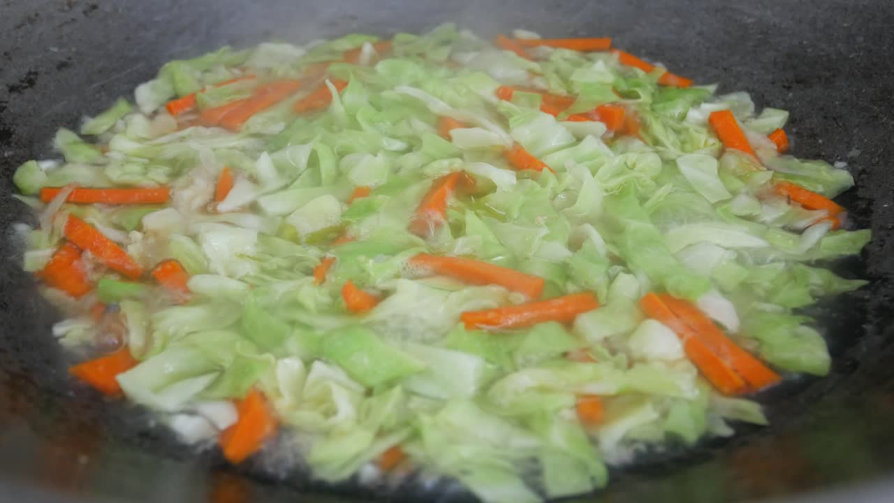 Fresh green cabbage is fried in a pan using hot cooking oil. Mix with carrot and chilli. Traditional Chinese cuisine