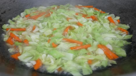 fresh green cabbage is fried in a pan using hot cooking oil. mix with carrot and chilli. traditional chinese cuisine