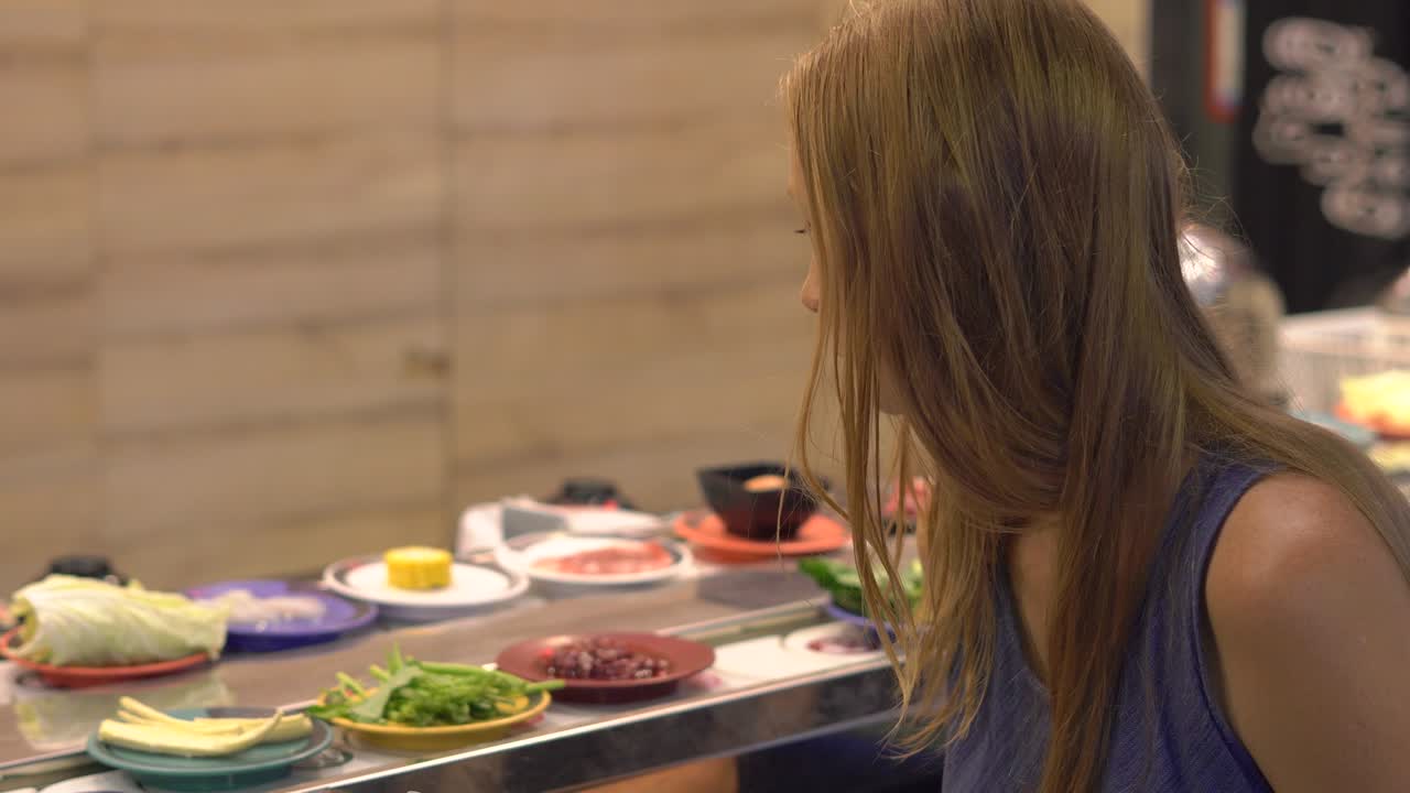 아시아 카페에서 젊은 여성은 뜨거운 비에 음식을 요리합니다. 음식은 작은 접시에 컨베이어에 제공됩니다. 음식 컨베이어.