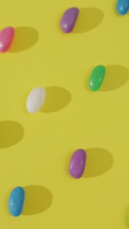 video of overhead view of rows of multi coloured sweets over yellow background