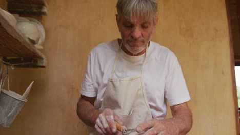 senior caucasian man wearing apron using potter's wheel in pottery workshop