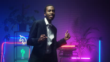 american young man in fancy suit dancing in room with neon lights